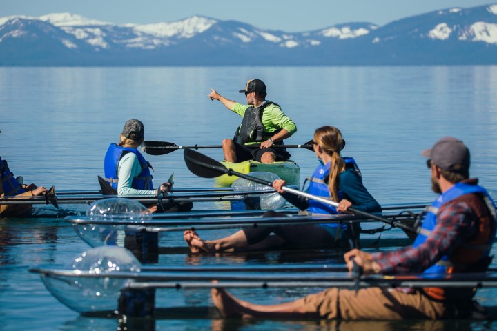 Group kayaking on clear lake with snowy mountains in background.