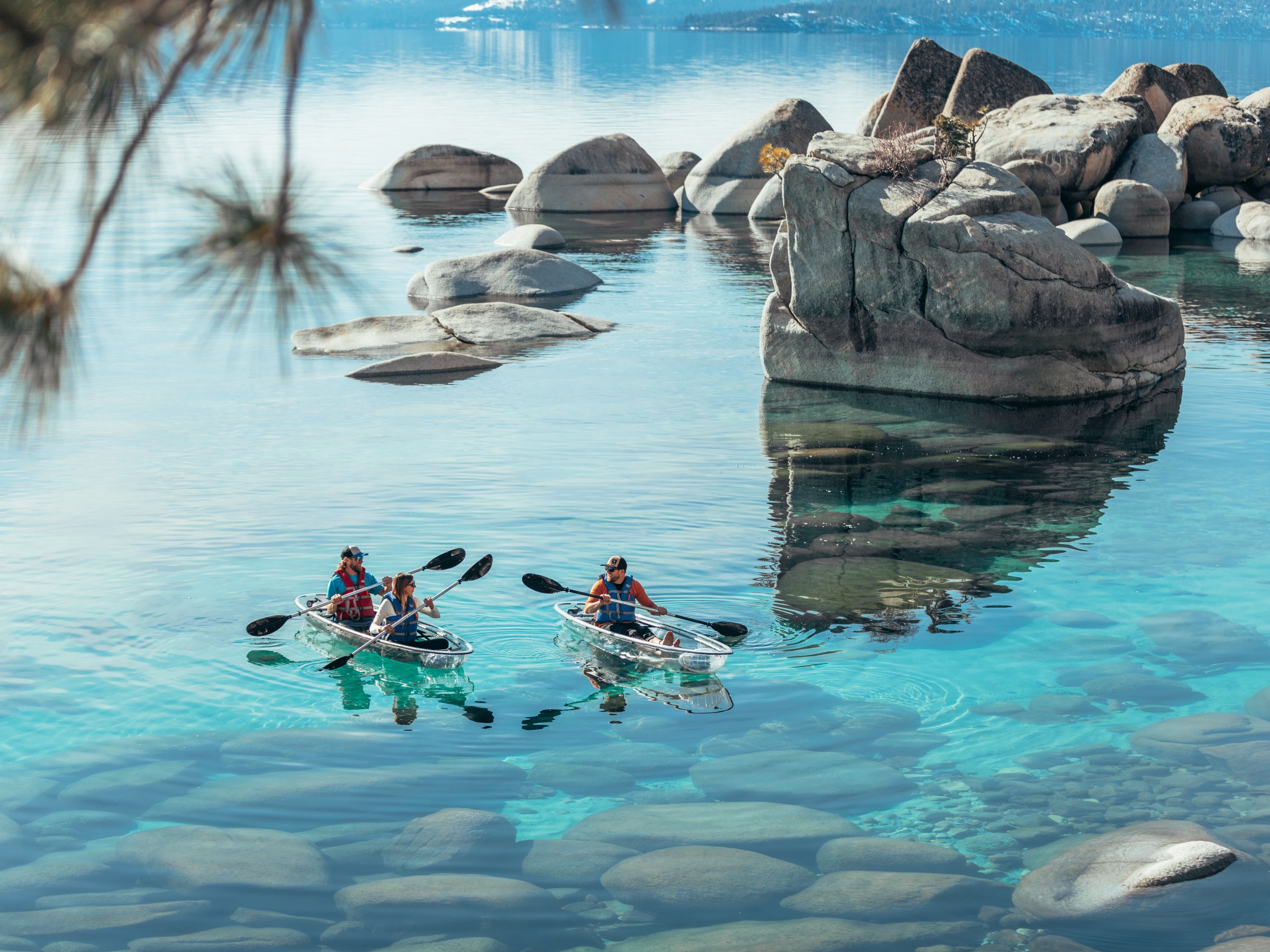 Two groups kayaking on clear, blue water with large rocks.