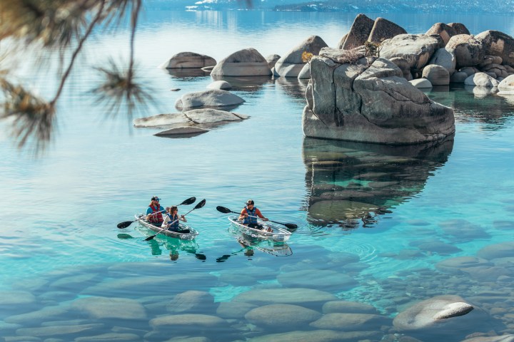Two groups kayaking on clear, blue water with large rocks.