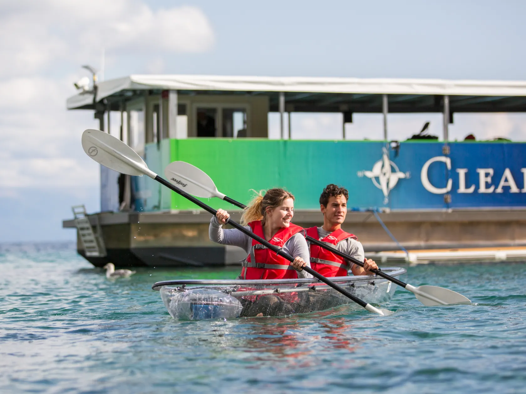 Two people kayaking in clear water near a boat.