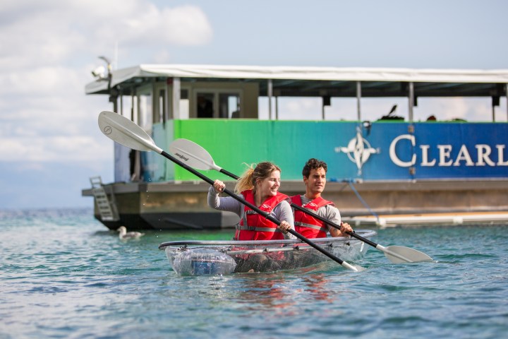 Two people kayaking in clear water near a boat.