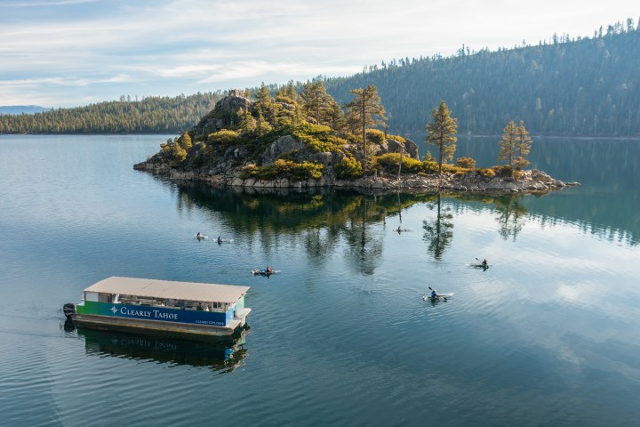 People kayaking on a lake near a wooded island, with a tour boat in the foreground.