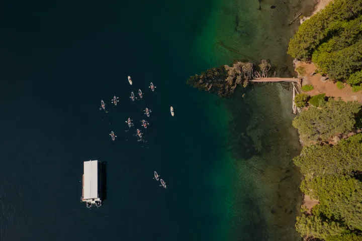 Aerial view of kayakers near a dock and trees on a lake.