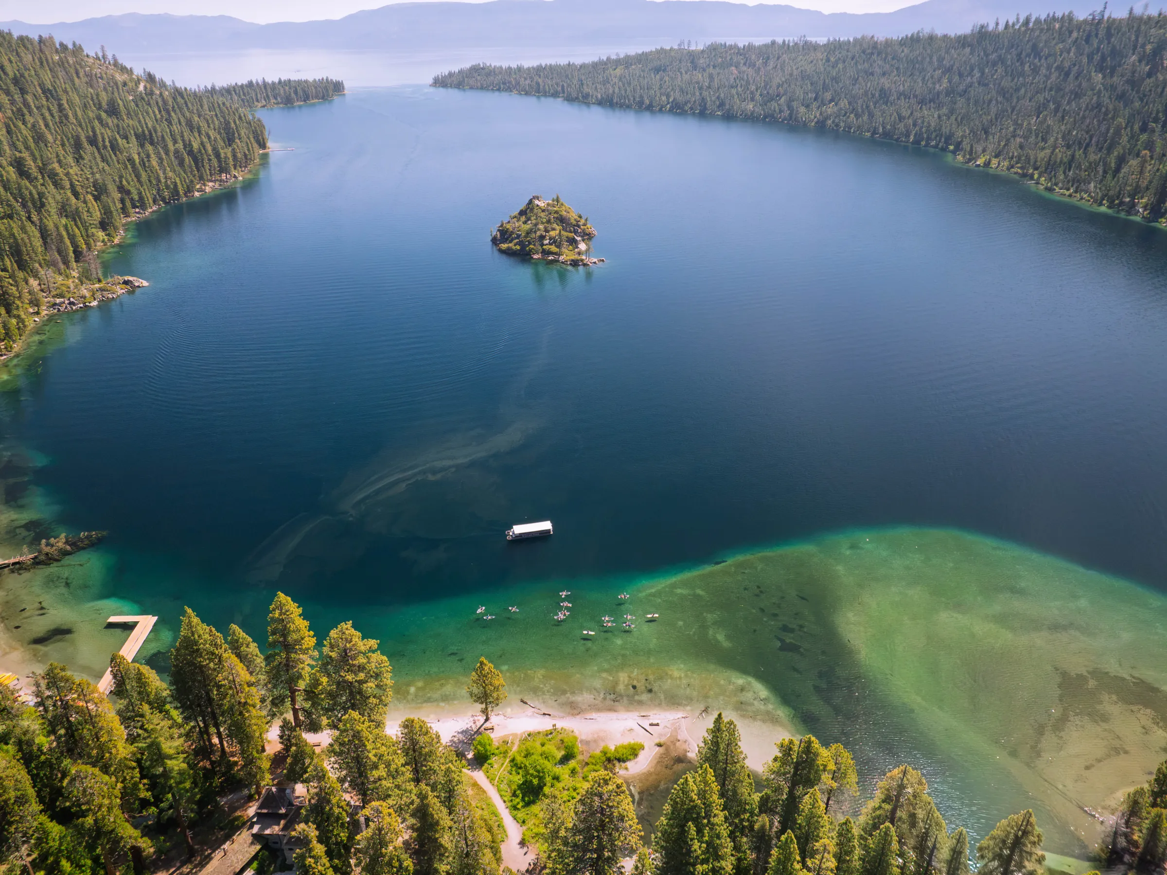 Aerial view of a clear lake with an island and surrounded by forested hills.