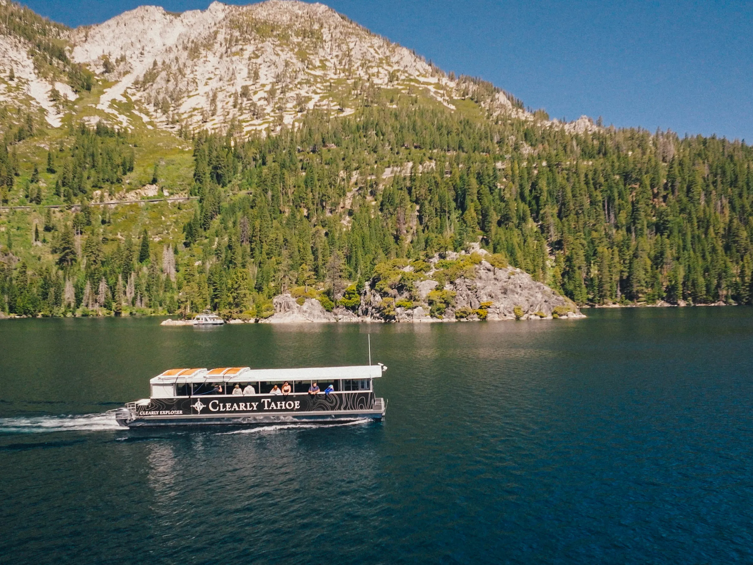 Boat on a lake with forested mountains in the background.