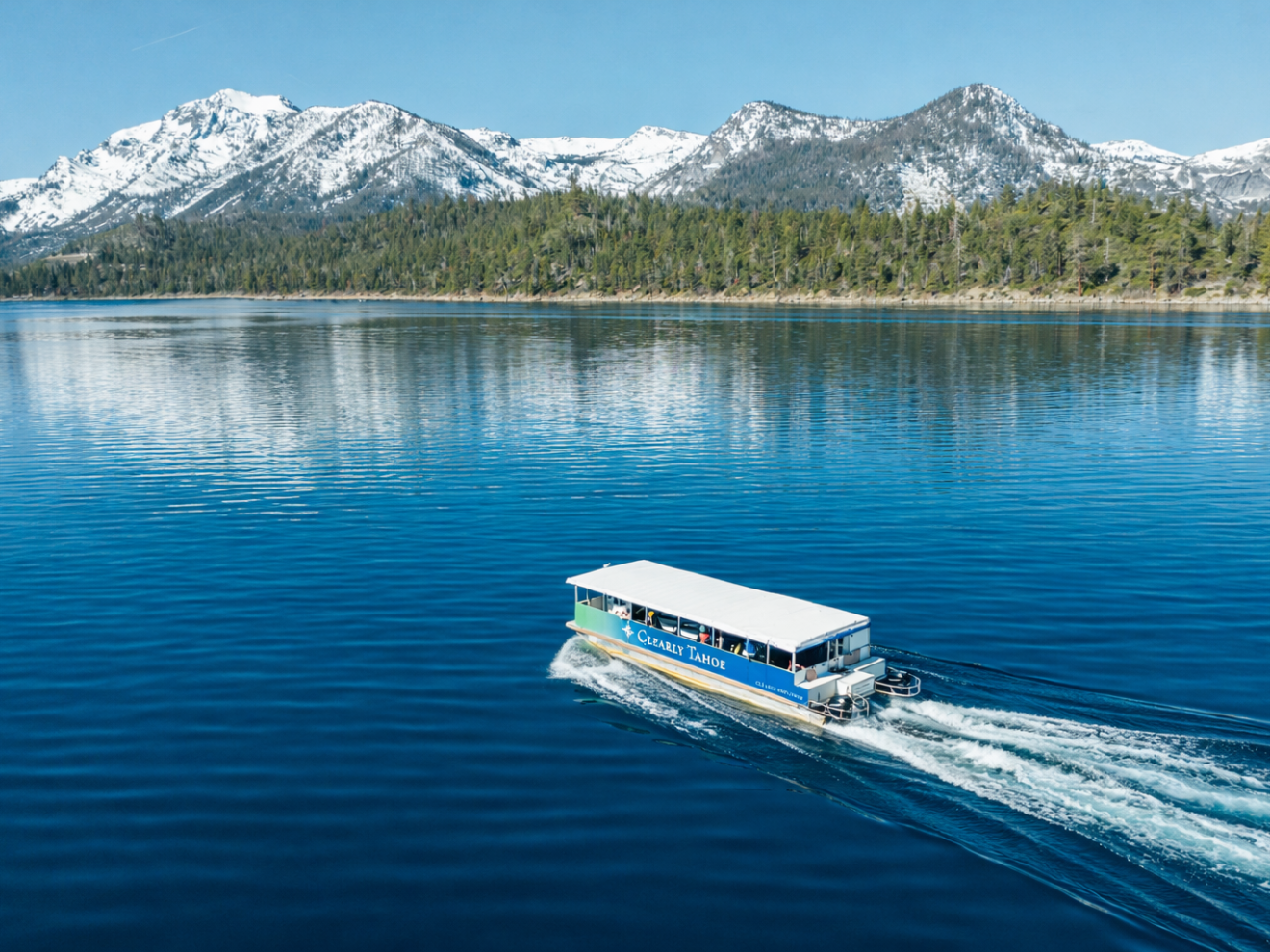 Boat on clear lake with snowy mountains in background, under clear blue sky.