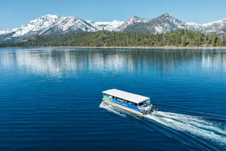 Boat on clear lake with snowy mountains in background, under clear blue sky.