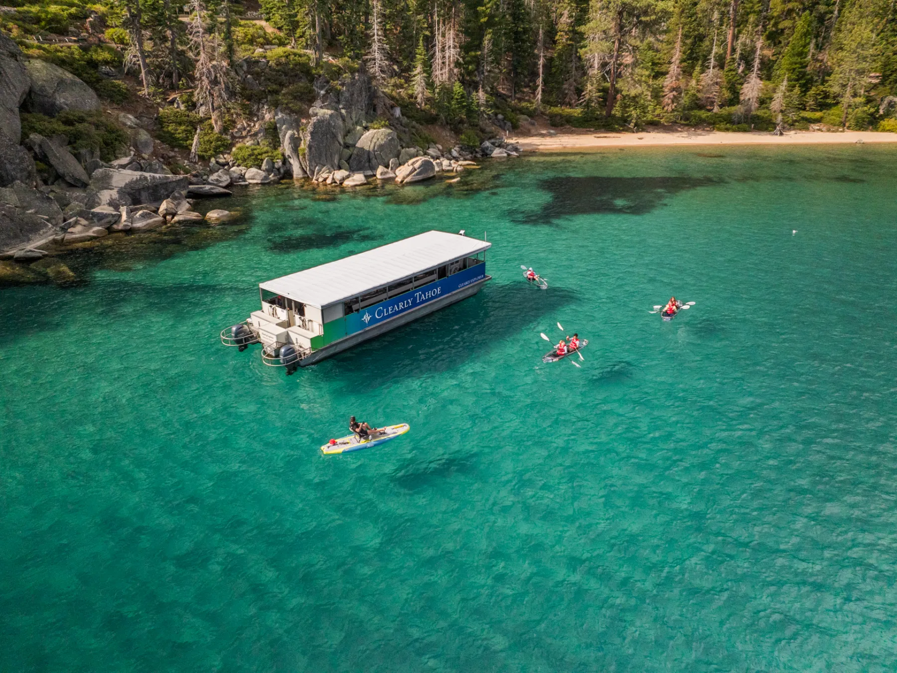 A boat and kayakers on clear turquoise lake with forested shoreline.