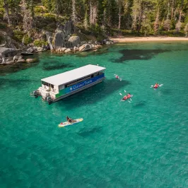 A boat and kayakers on clear turquoise lake with forested shoreline.