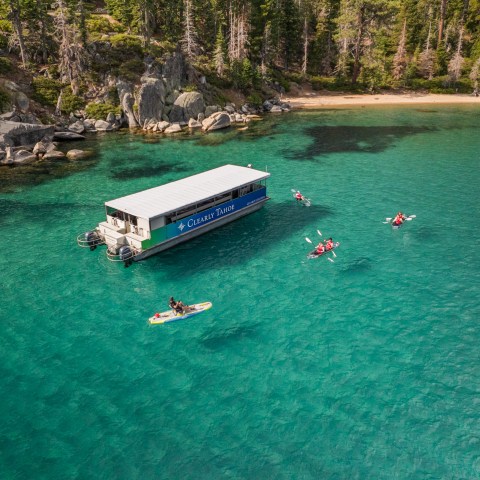 A boat and kayakers on clear turquoise lake with forested shoreline.