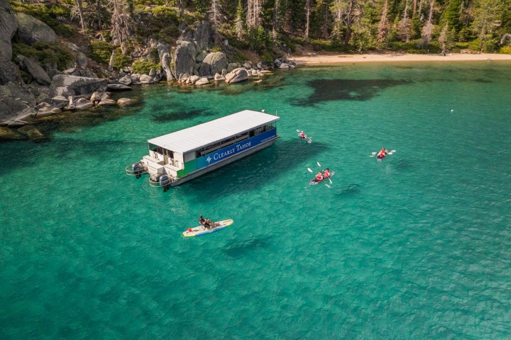 A boat and kayakers on clear turquoise lake with forested shoreline.