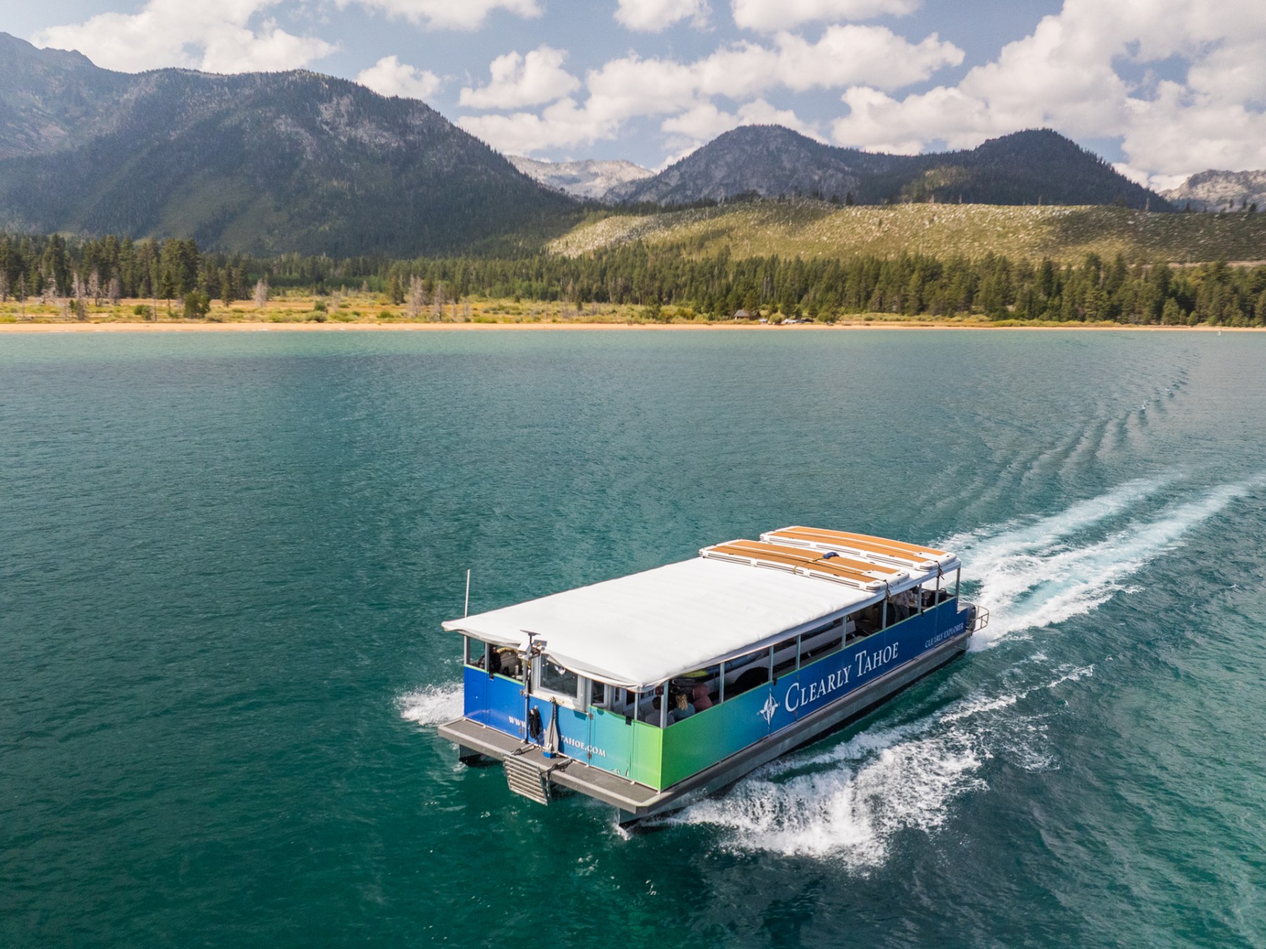 Boat on a lake with mountainous landscape and trees in the background under a cloudy sky.