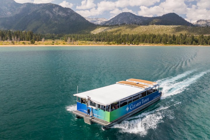 Boat on a lake with mountainous landscape and trees in the background under a cloudy sky.