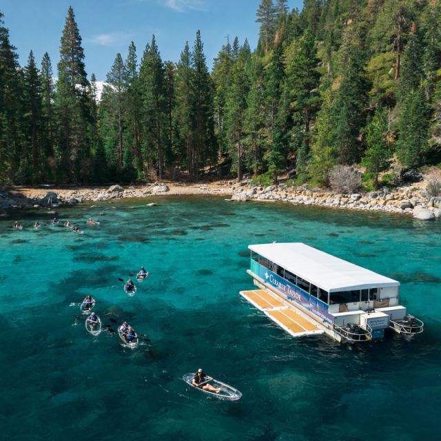 Boat and kayaks on turquoise lake with pine forest shoreline.