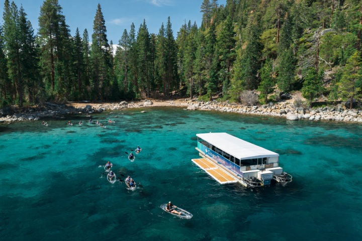 Boat and kayaks on turquoise lake with pine forest shoreline.