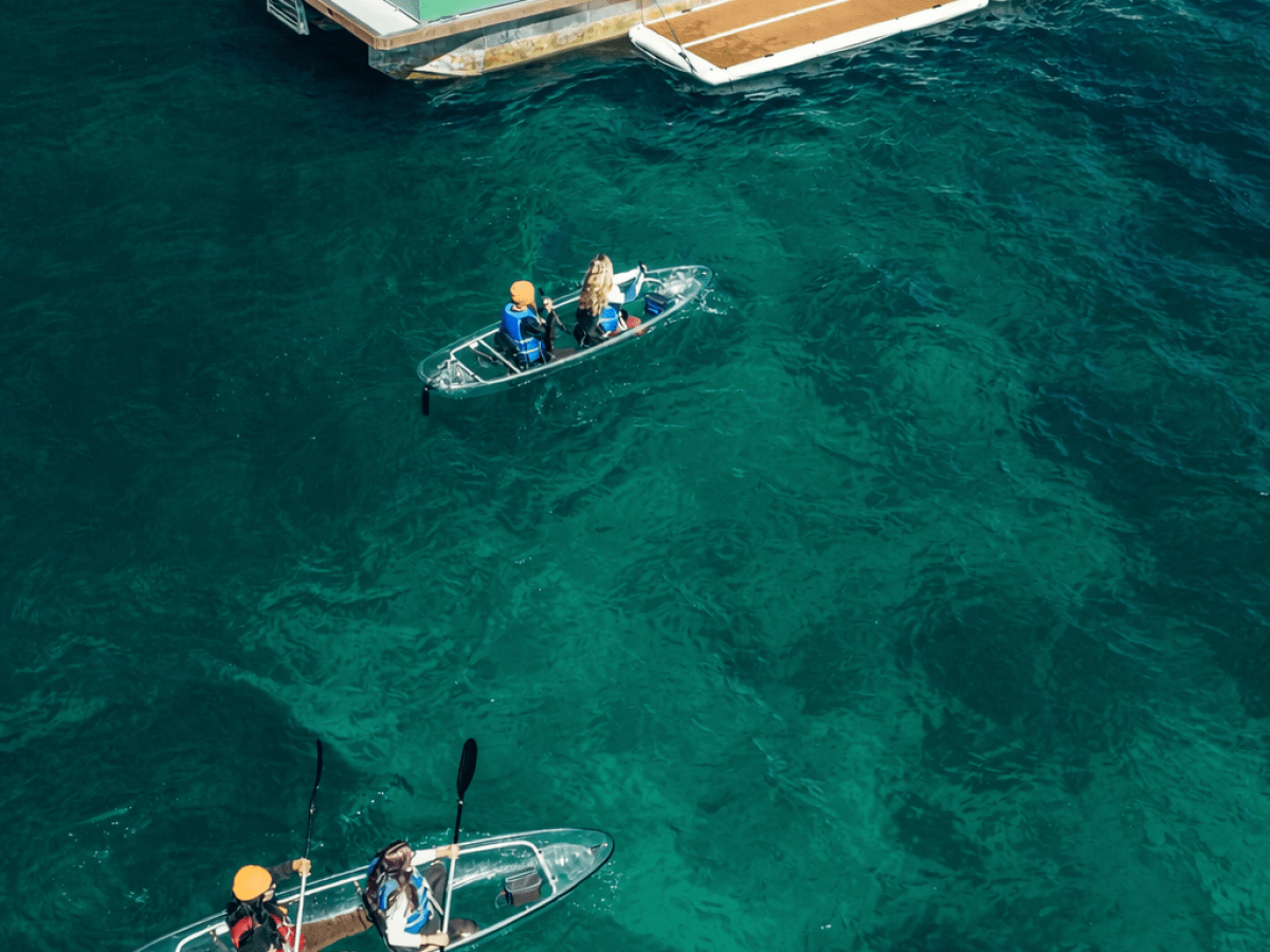 Two clear kayaks near a boat with 'Clearly Tahoe' sign on turquoise water.