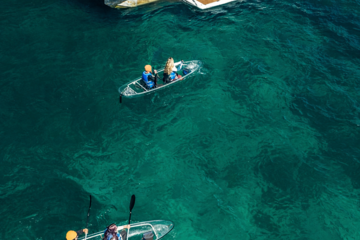 Two clear kayaks near a boat with 'Clearly Tahoe' sign on turquoise water.