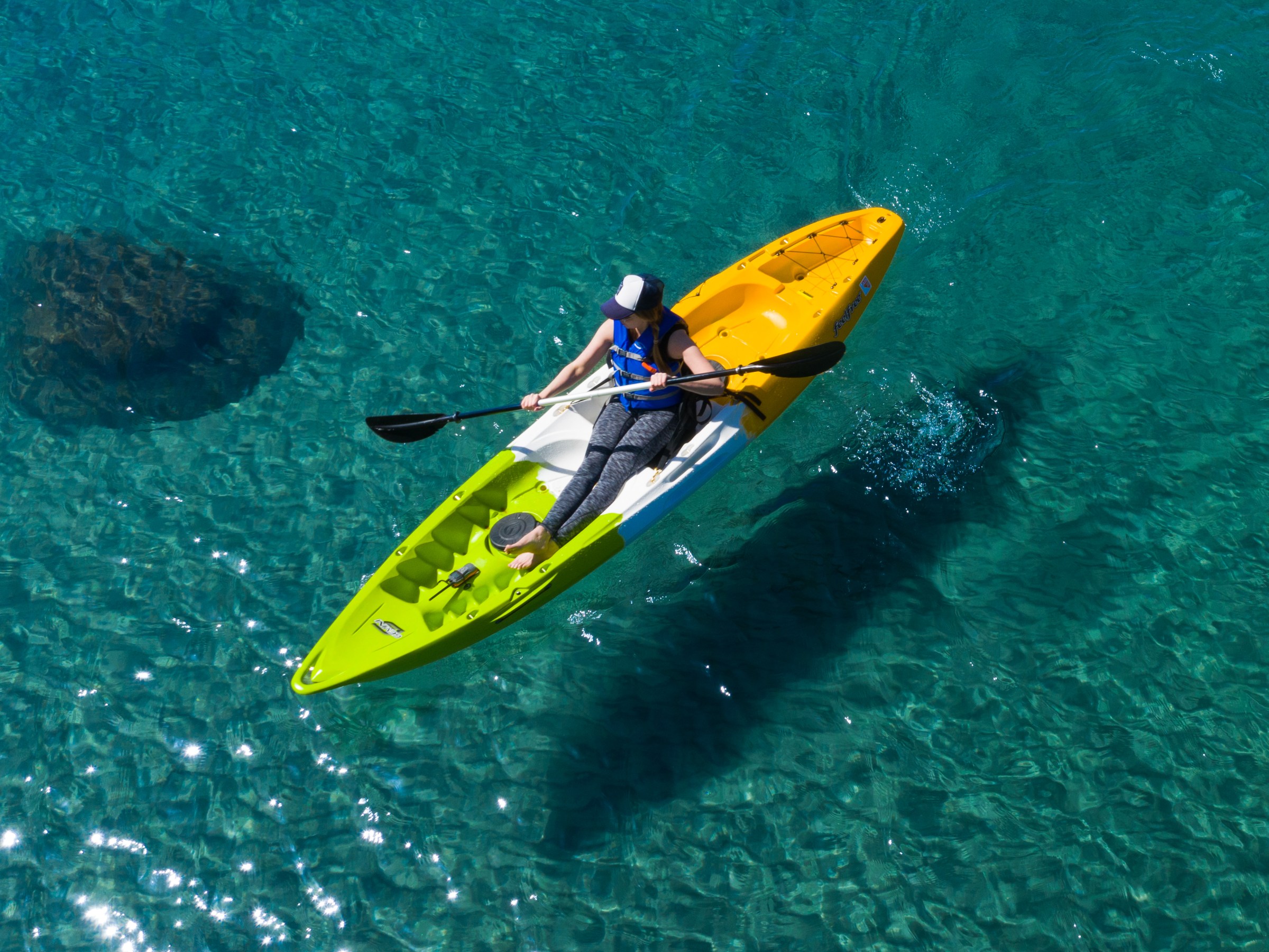 Person kayaking on clear turquoise water with visible rock below.