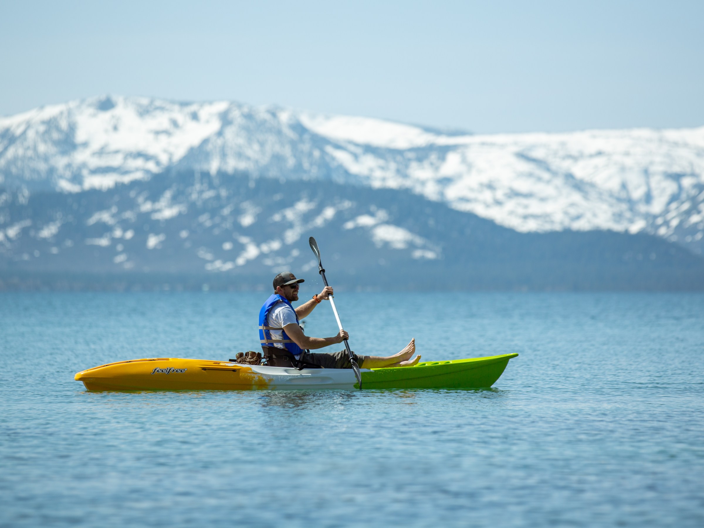 Man kayaking on a lake with snow-capped mountains in the background.