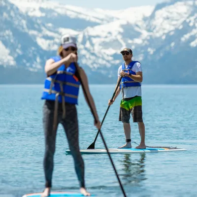 Two people paddleboarding on a lake with snowy mountains in the background.