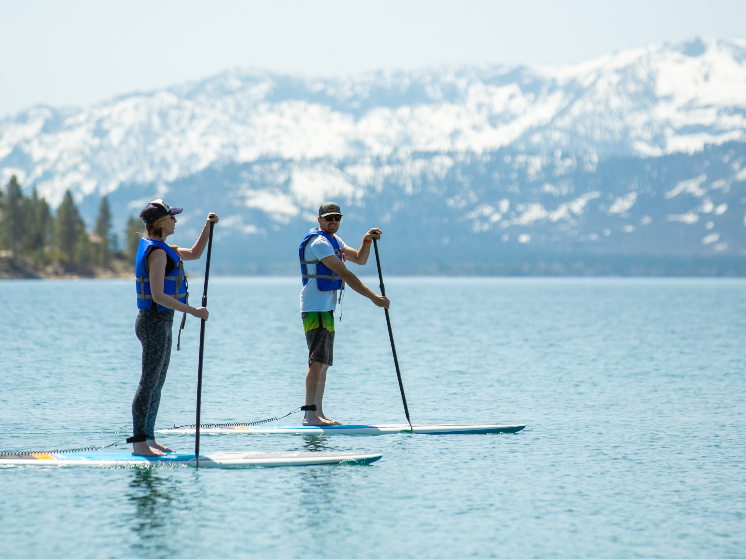 Two people paddleboarding on a lake with snowy mountains in the background.