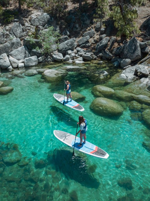 Two people paddleboarding on a clear, rocky, turquoise river.