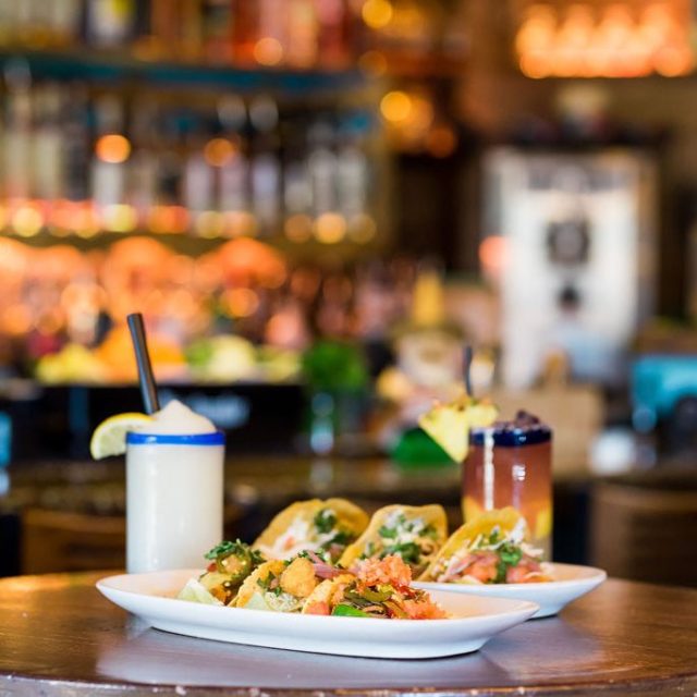 Tacos and drinks on a wooden table in a restaurant setting.