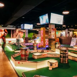 Indoor mini-golf course with colorful decor and overhead screens.