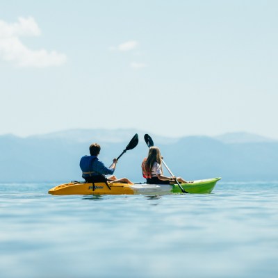 Two people kayaking on a calm lake with mountains in the background.