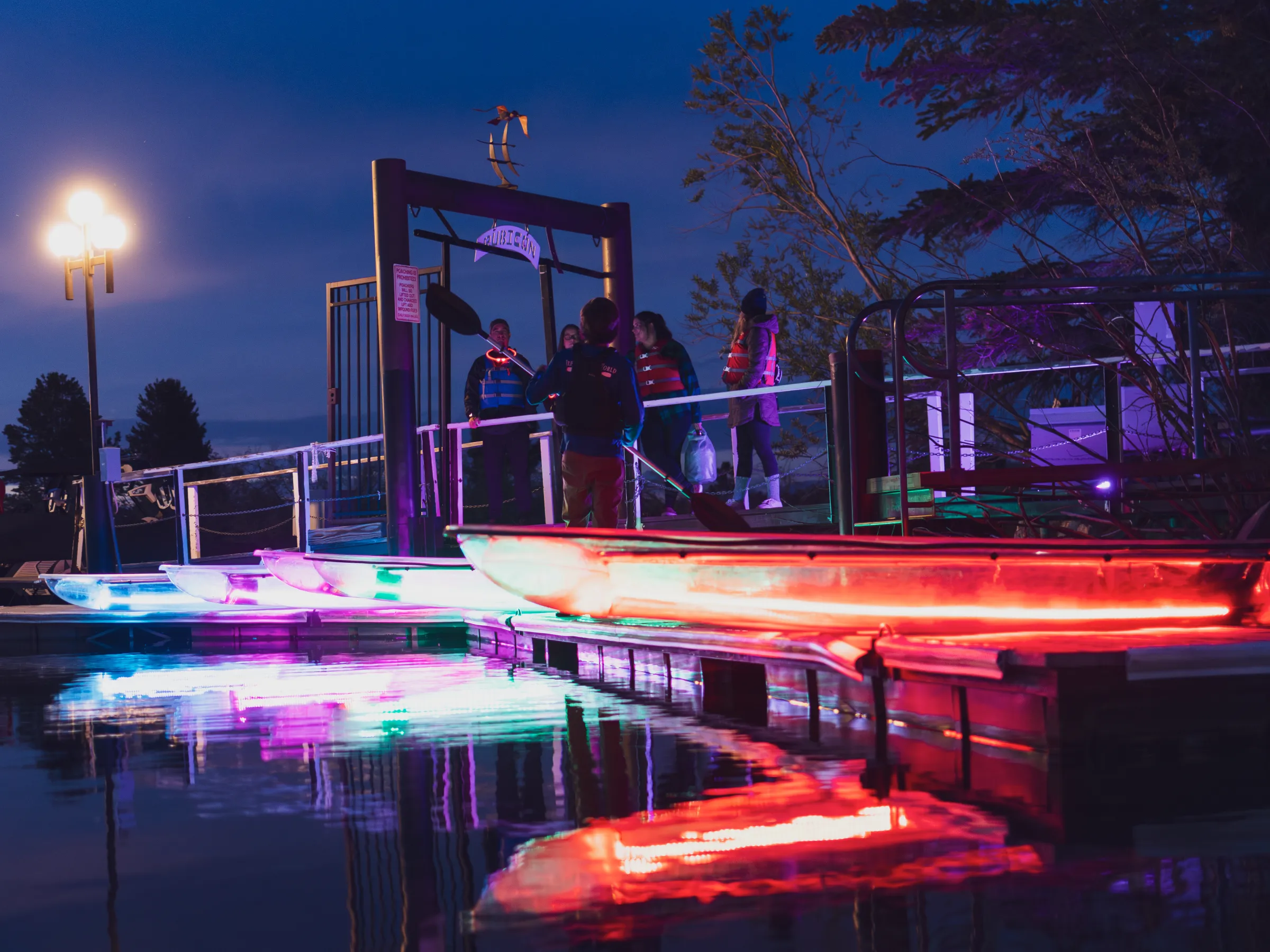 Docked boats illuminated by colorful lights at night.