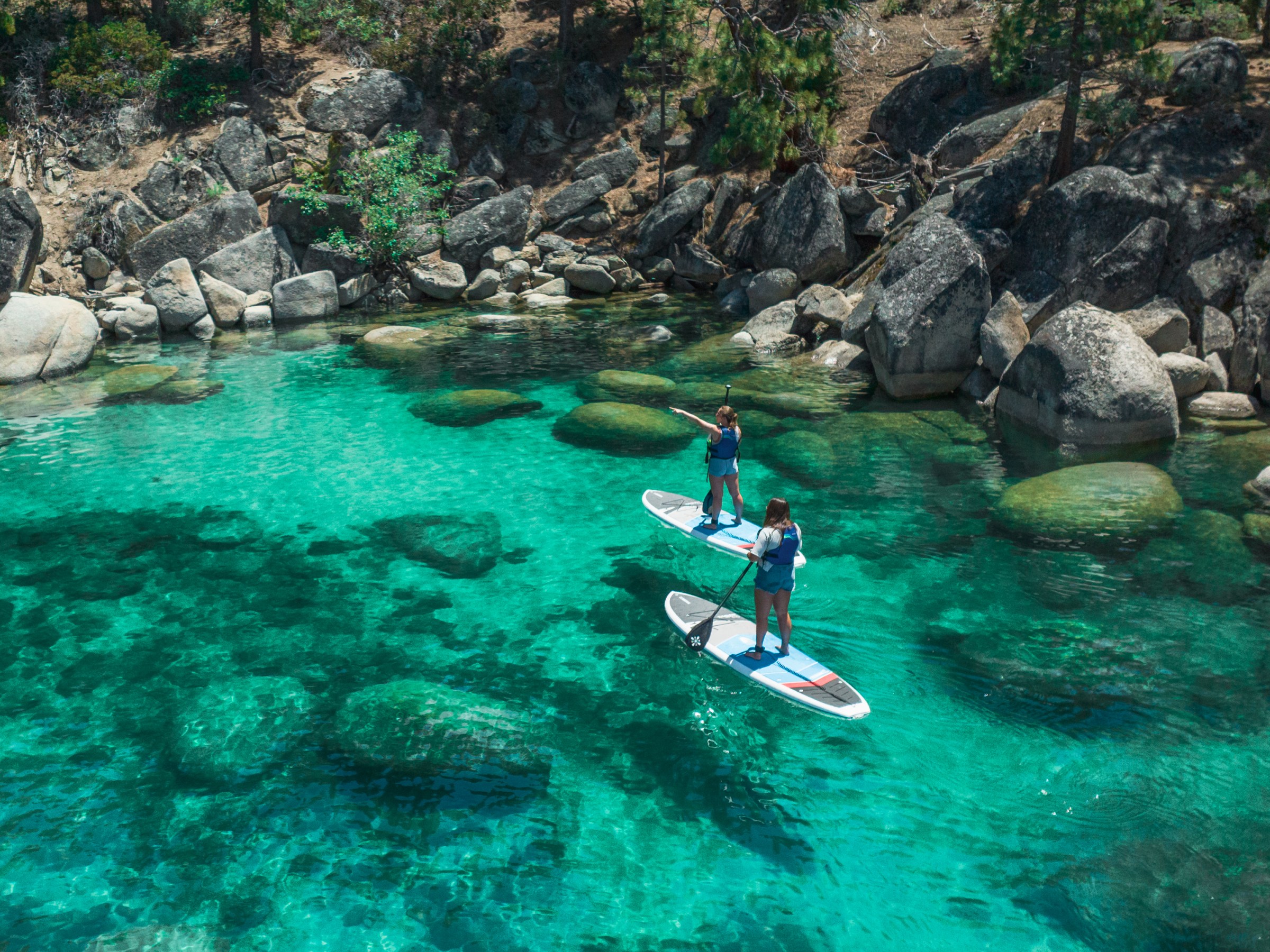 Two people paddleboarding on clear turquoise water surrounded by rocks.