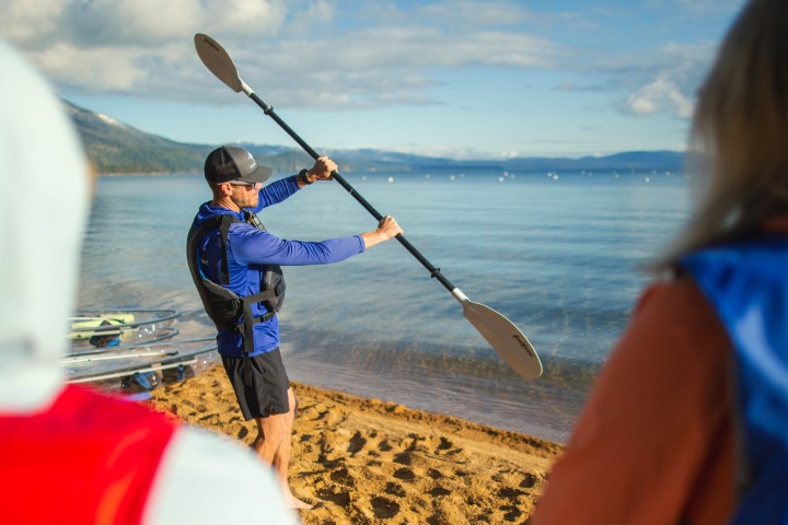 Kayaking instructor on sandy beach demonstrating paddle techniques.