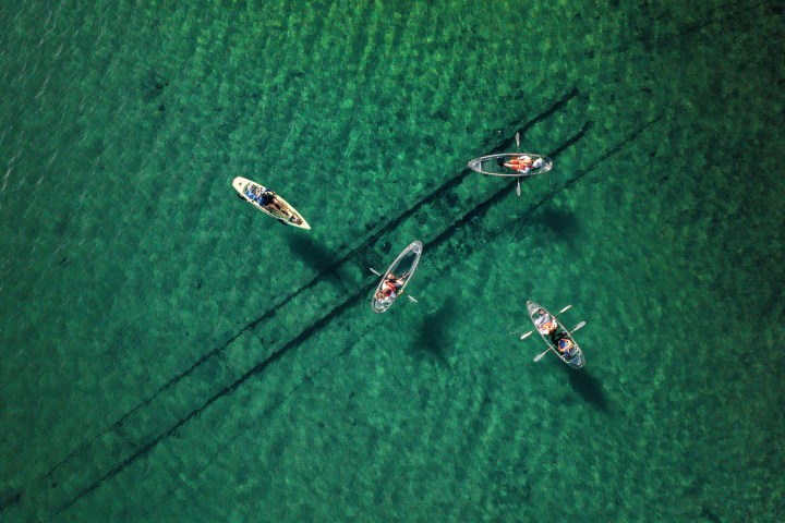 Four kayaks with people on clear green water viewed from above.