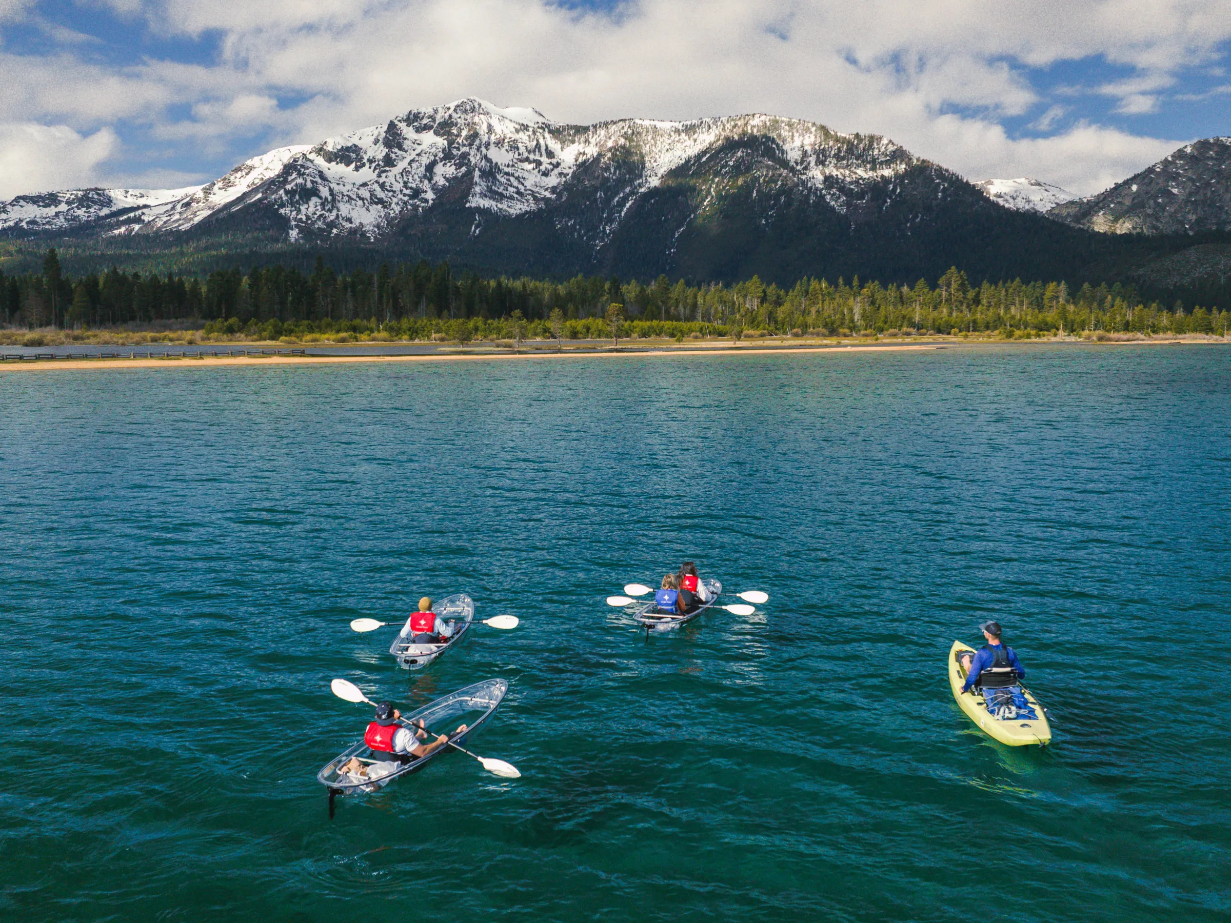 Four kayakers on a lake with snowy mountains in the background.