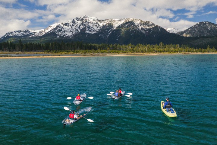 Four kayakers on a lake with snowy mountains in the background.