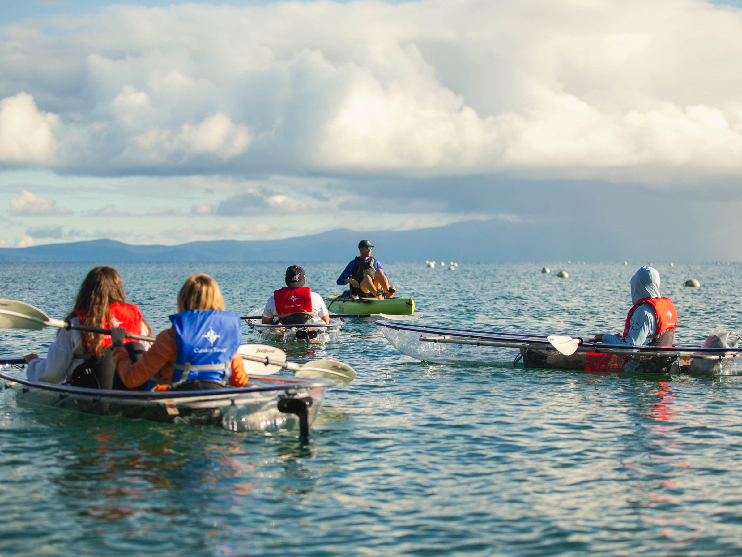 Group of people kayaking on a calm sea under a cloudy sky.