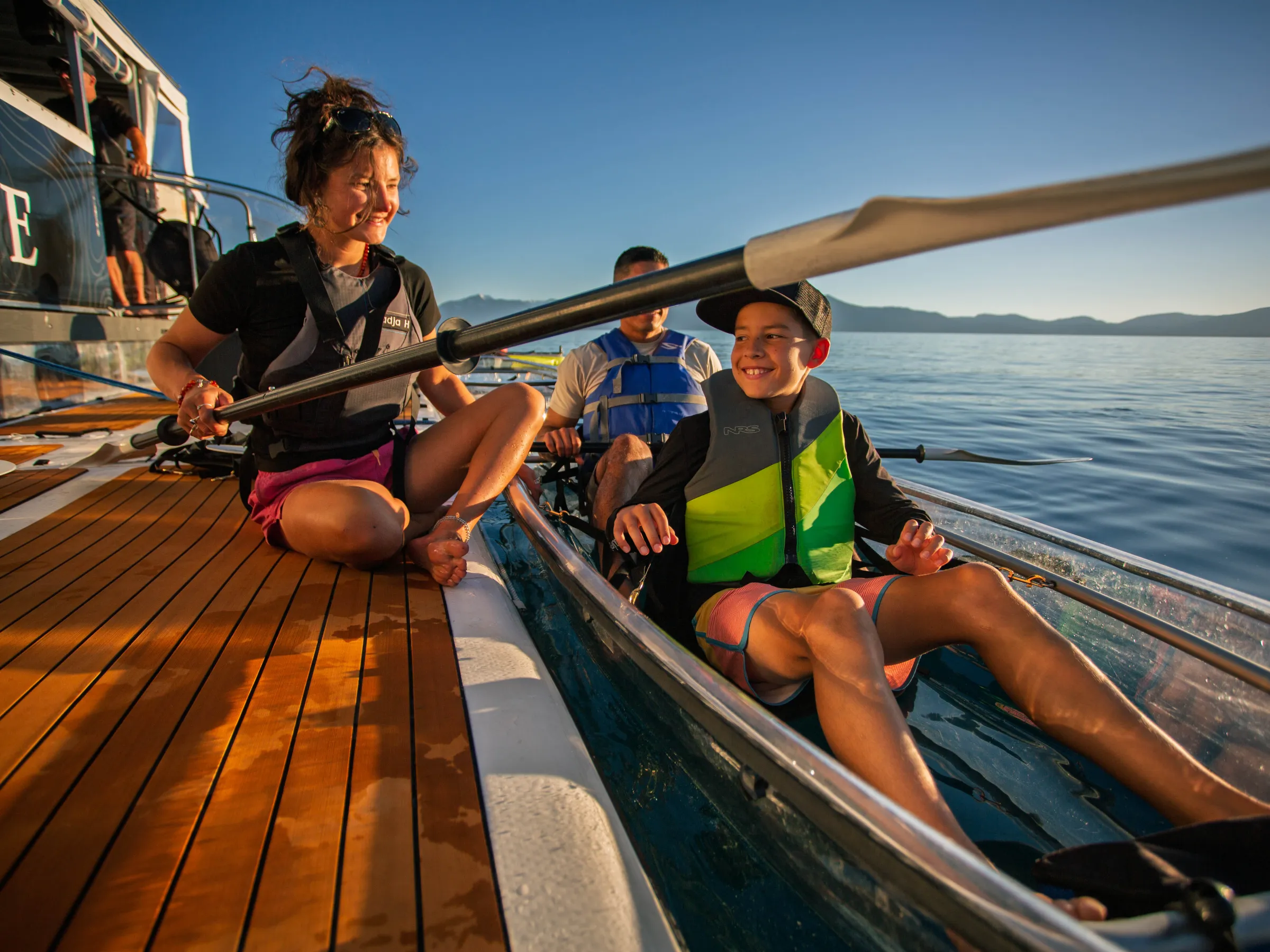 Smiling woman and child in kayak on sunny lake near boat.