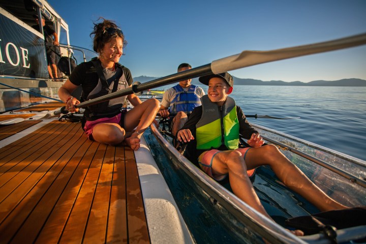 Smiling woman and child in kayak on sunny lake near boat.