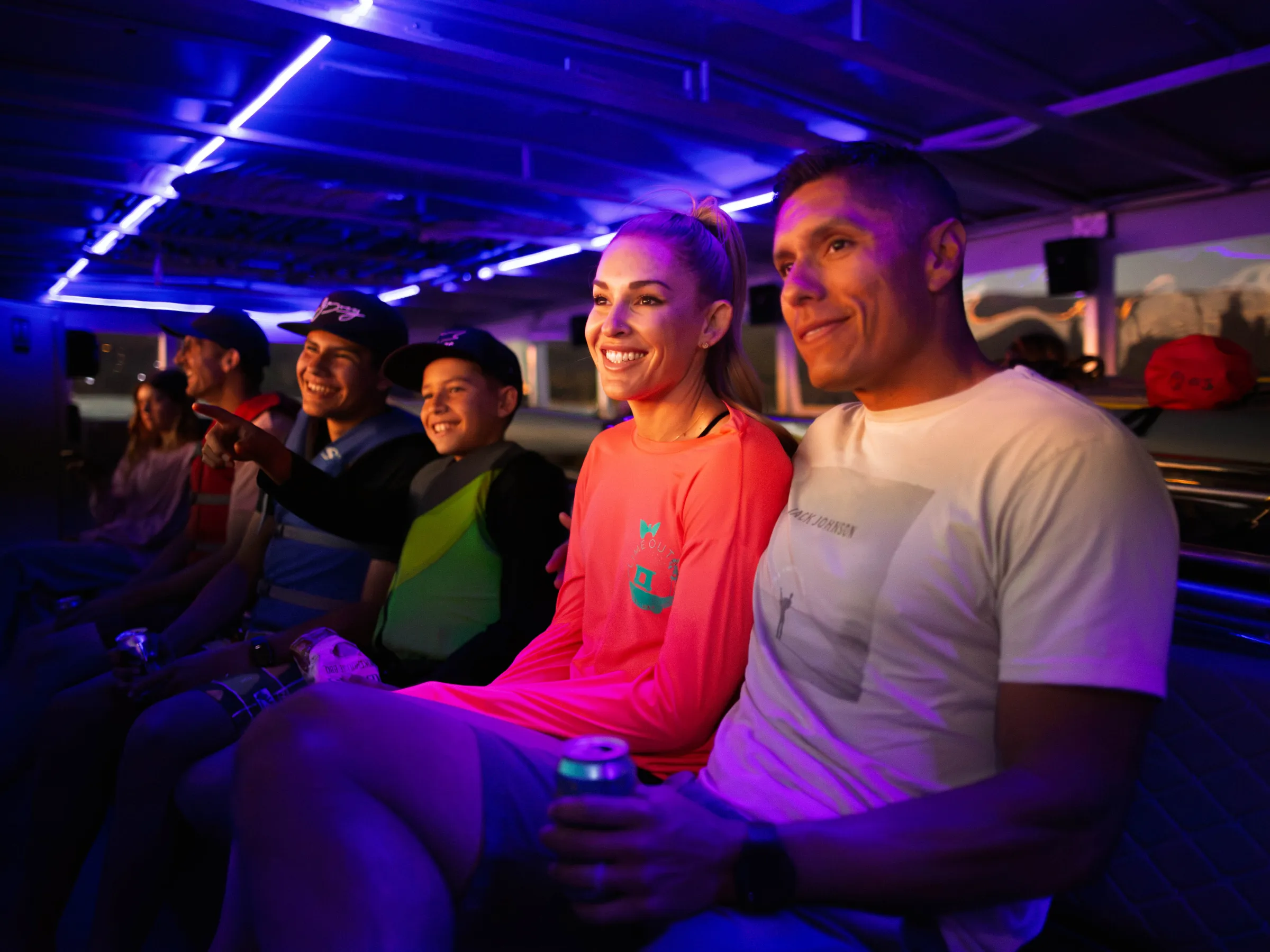 Group of people smiling and sitting on a bench under purple LED lights.