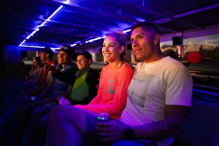 Group of people smiling and sitting on a bench under purple LED lights.