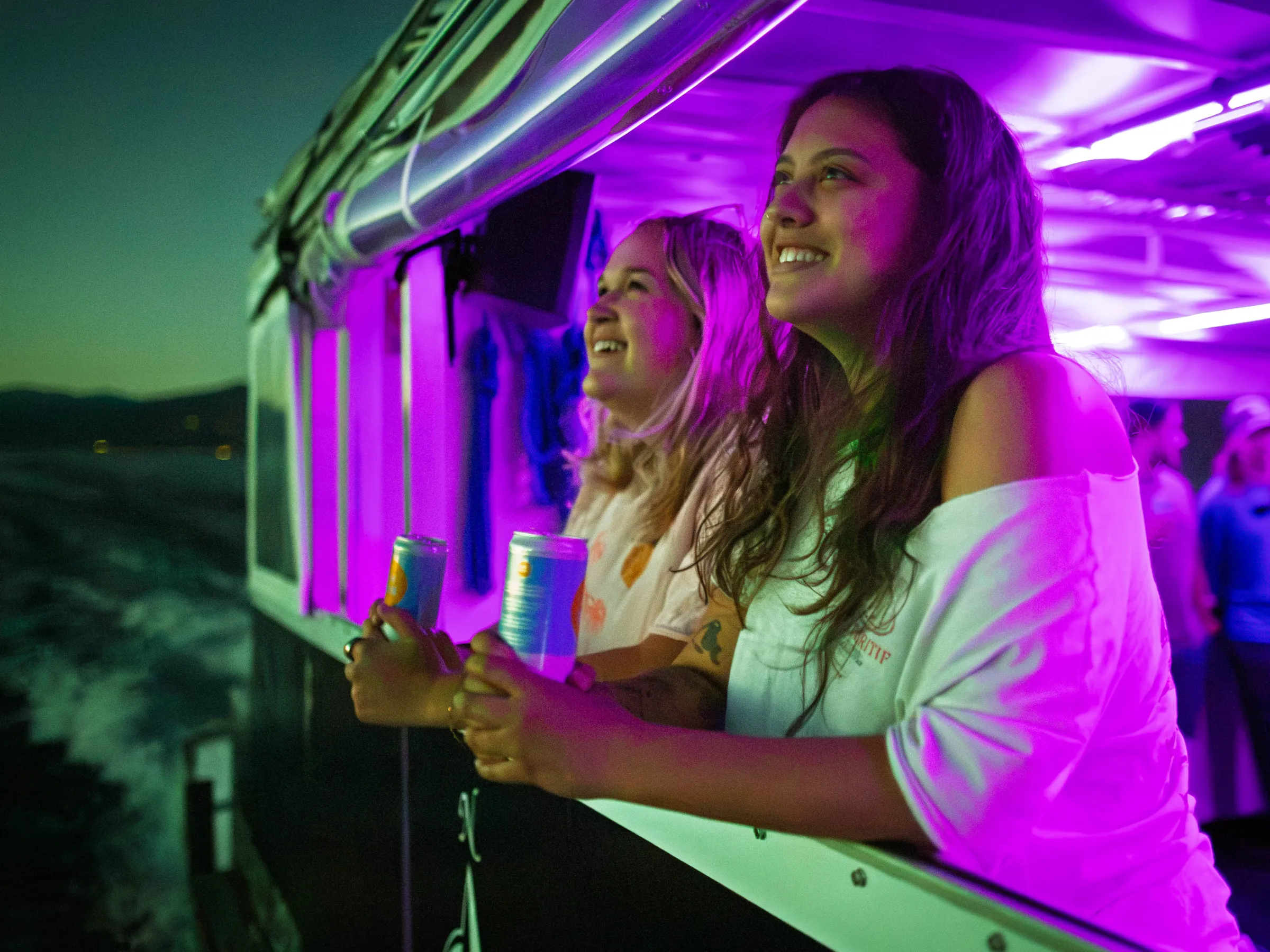Two people smiling on a boat at night holding drinks.