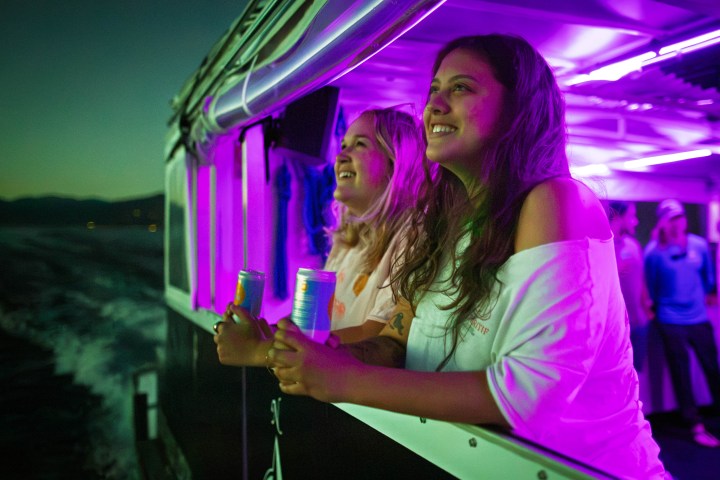 Two people smiling on a boat at night holding drinks.