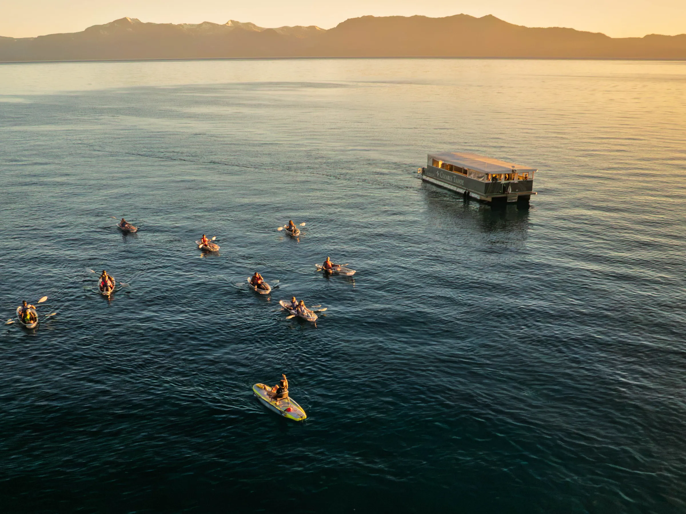 Groups of kayakers on a lake near a dock at sunset.