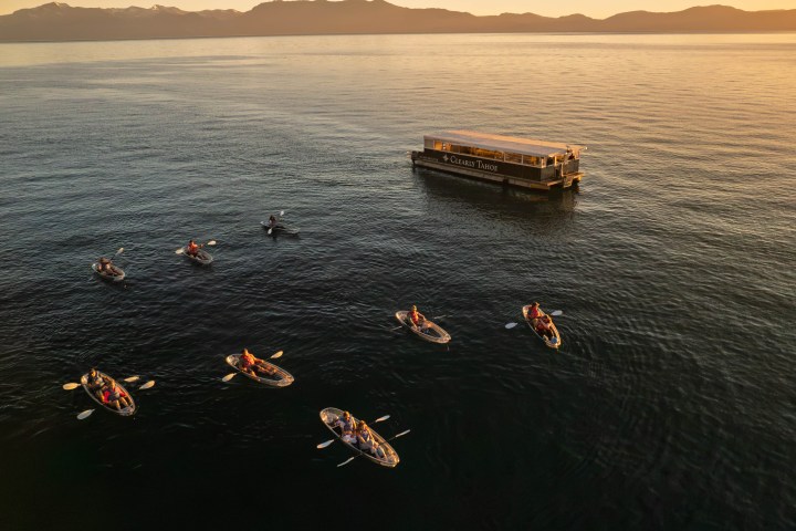Kayakers near a large boat at sunset on a calm lake with mountains in the background.