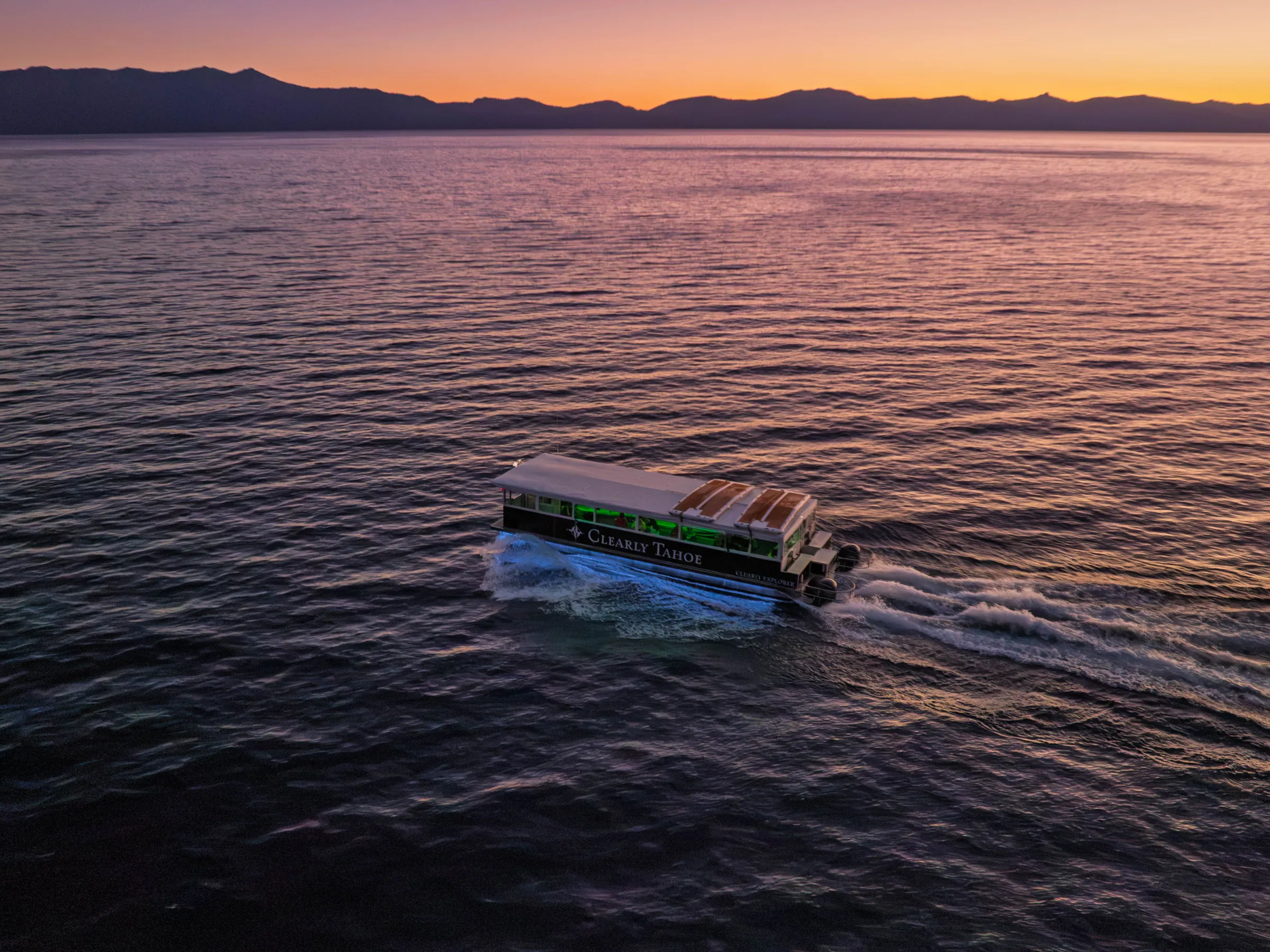 Boat on a calm lake at sunset with mountains in the background.
