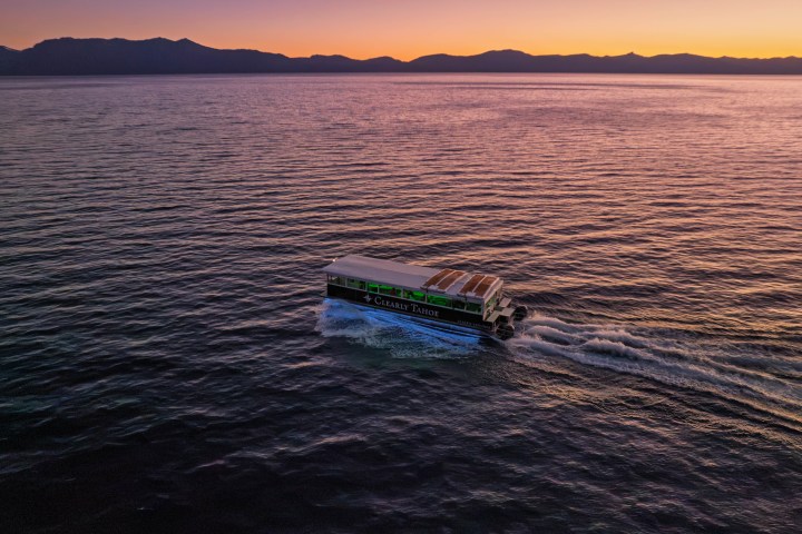 Boat on a calm lake at sunset with mountains in the background.