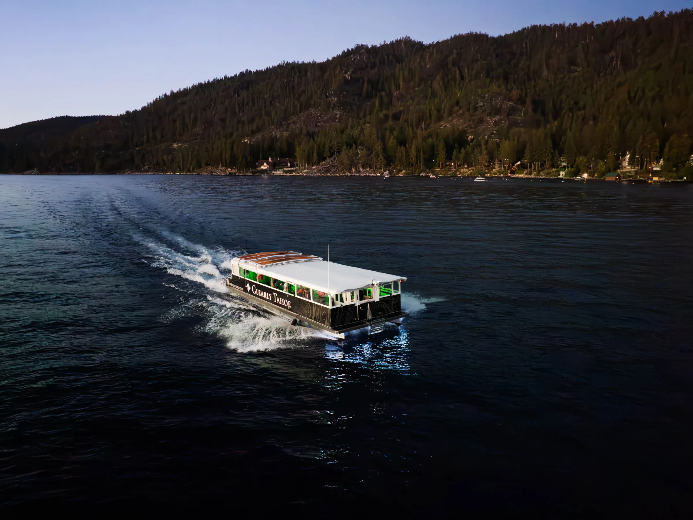 Boat cruising on a lake with forested hills in background.