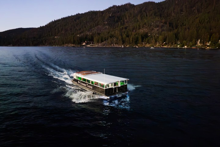 Boat cruising on a lake with forested hills in background.