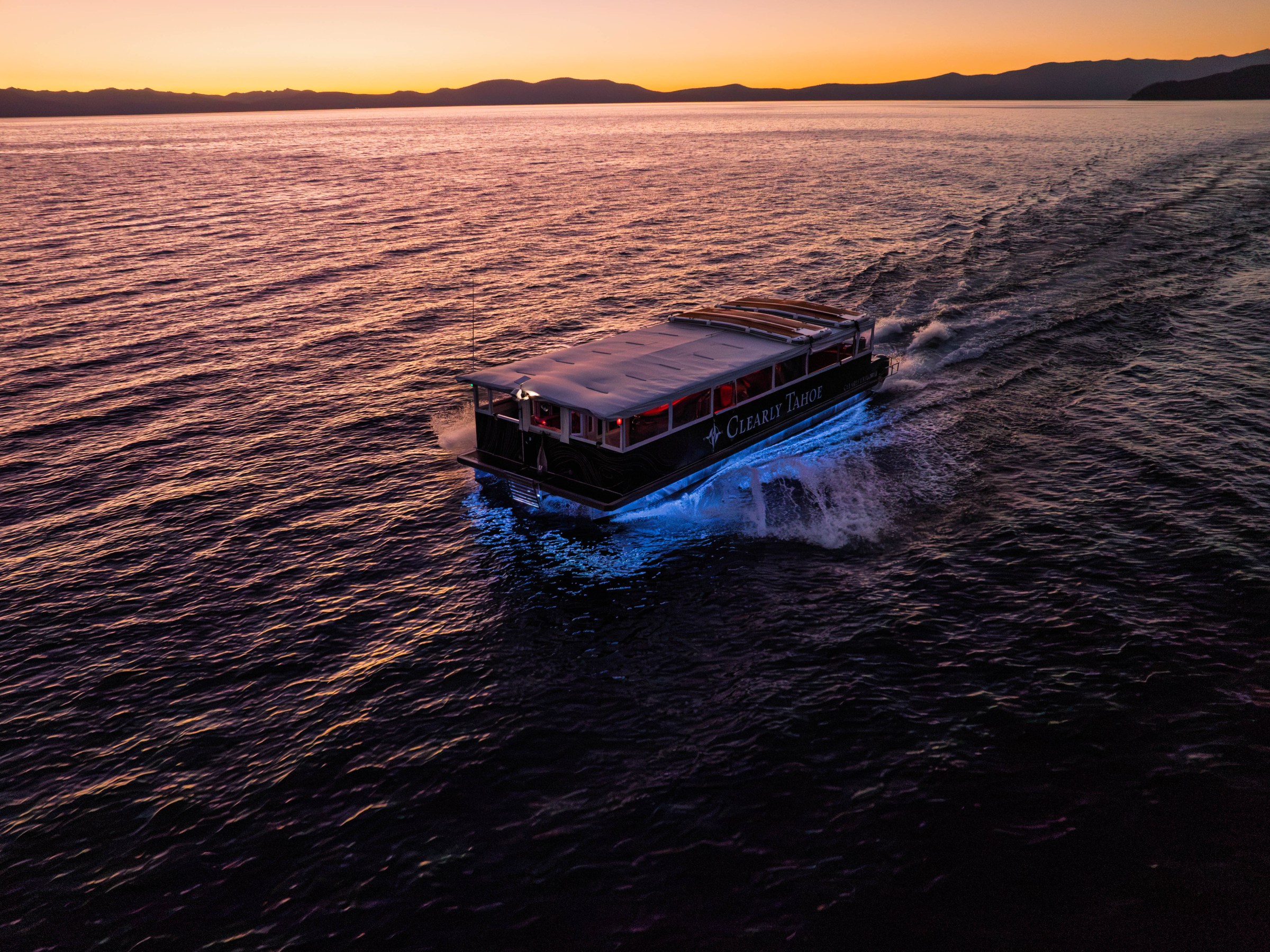 Boat with blue lights on water at sunset, mountainous horizon.