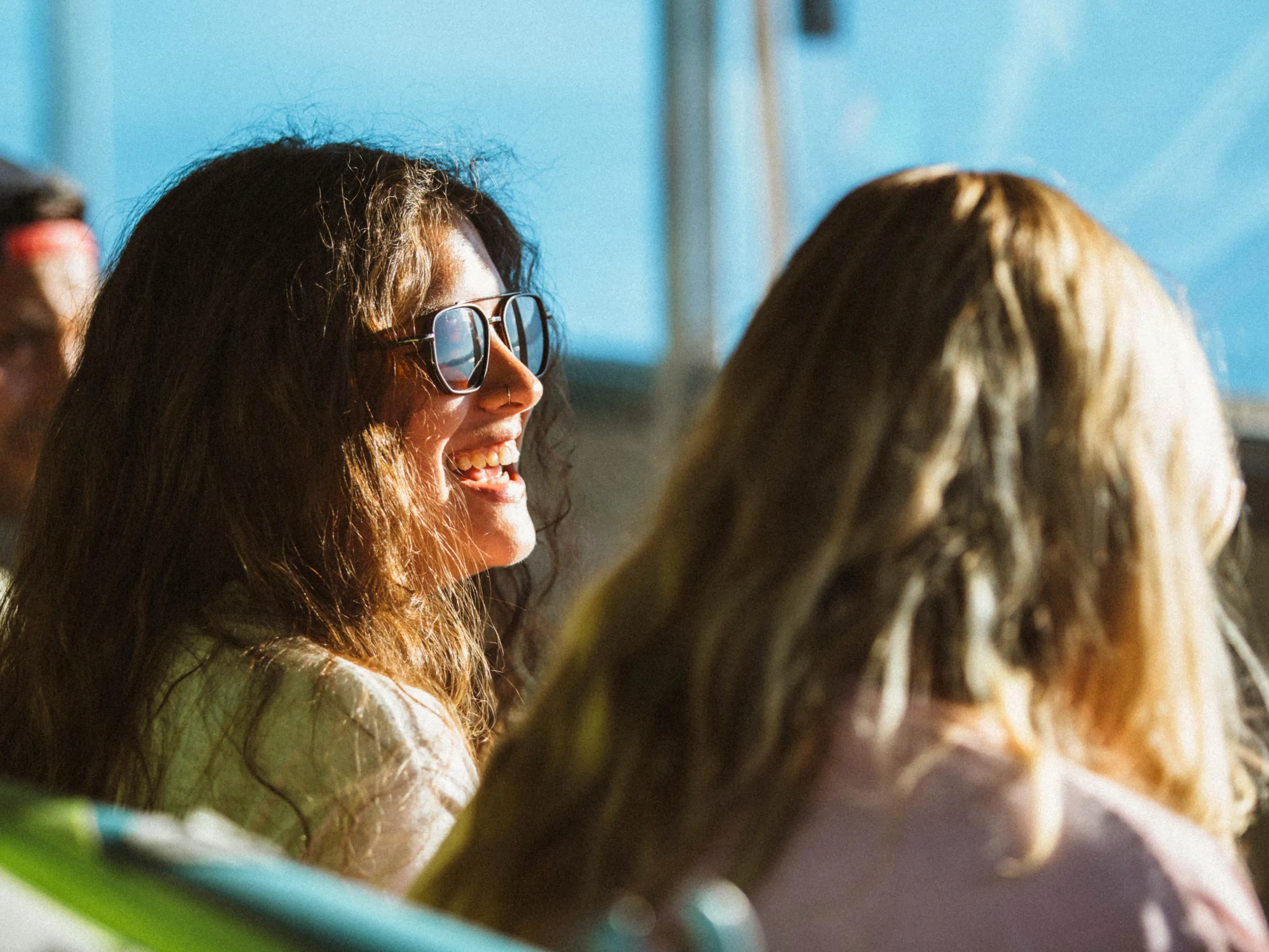 Two women are sitting on a bus, sunlight shining on them.